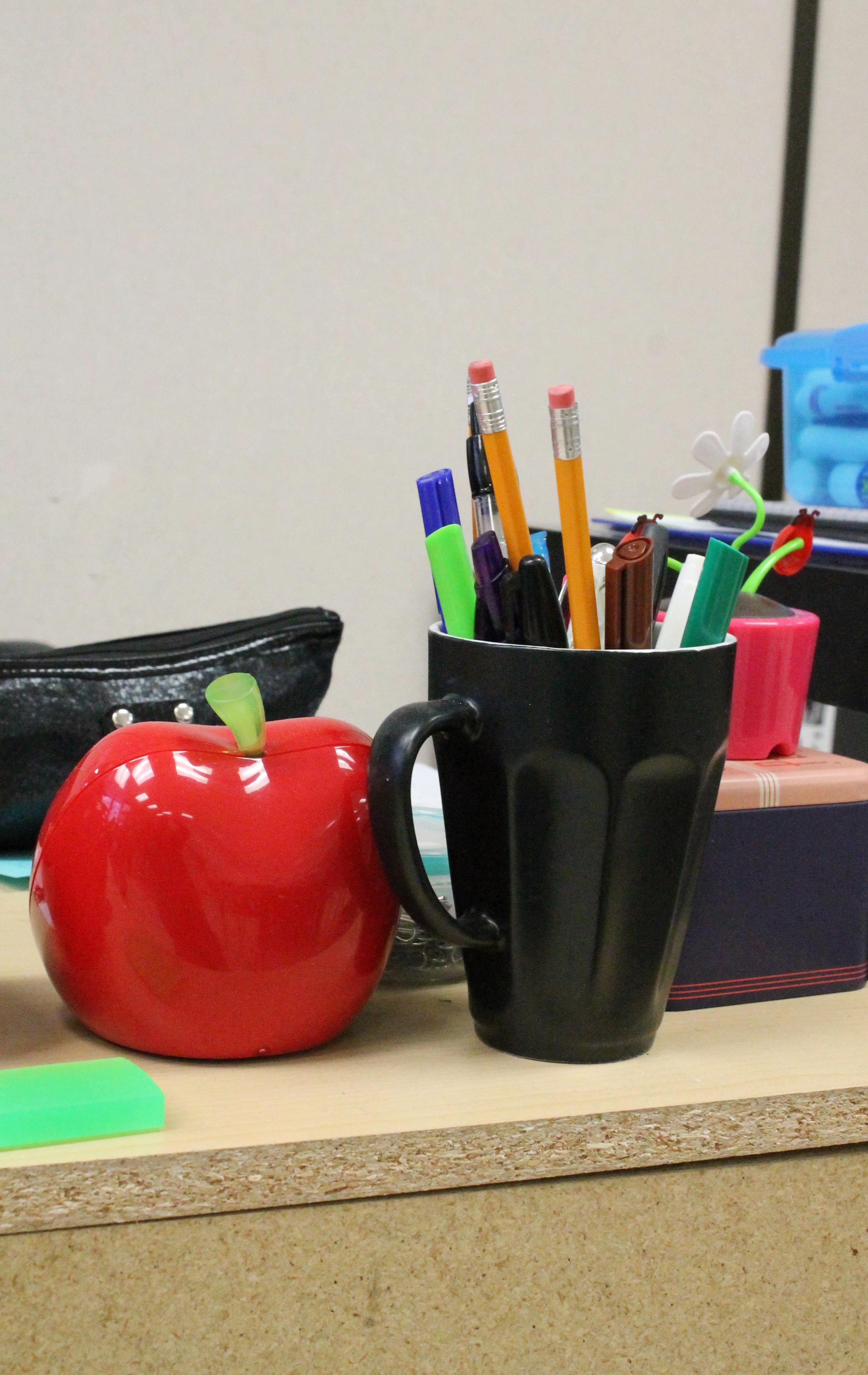 An apple and a mug of pens and pencils sits on a desk